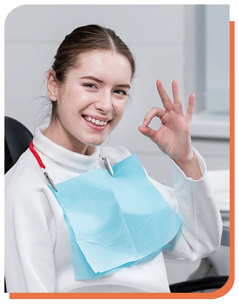 Young patient smiling and giving an OK sign while wearing a dental bib.