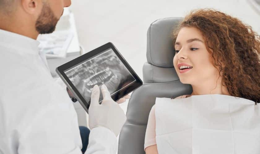 Dentist reviewing dental X-rays with patient in treatment chair.
