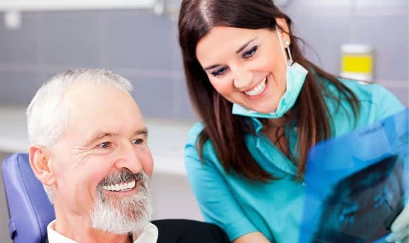 Smiling dentist with female patient in dental office discussing implant benefits.