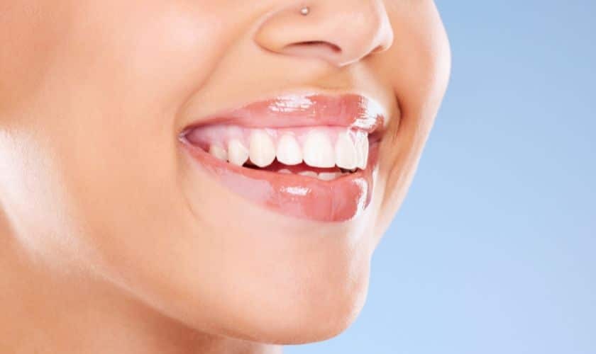 Woman with bright white teeth smiling against blue background, showcasing cosmetic dental results.