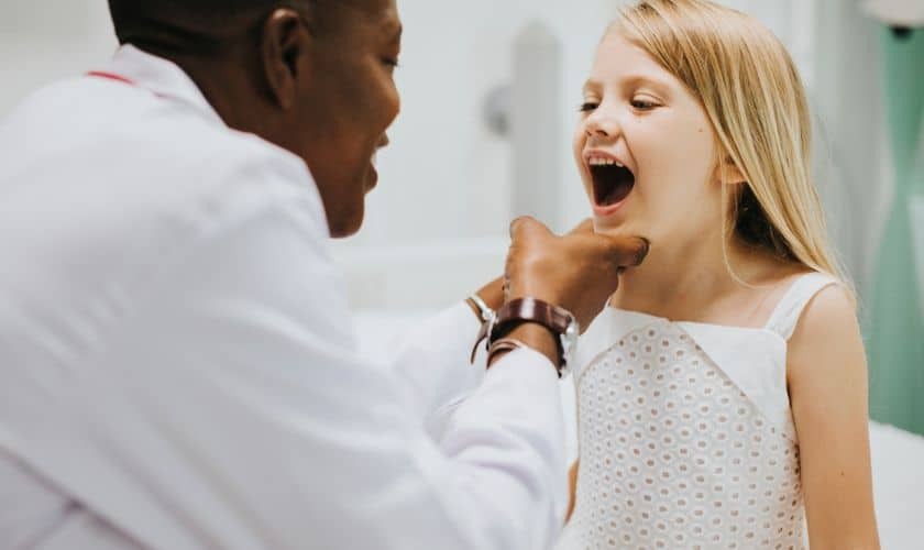 Pediatric dentist examining a young girl's teeth during a dental checkup appointment.