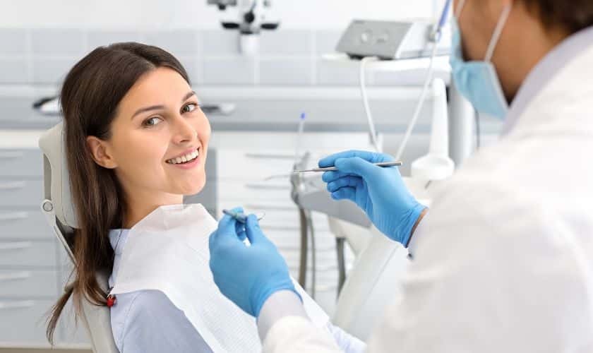 Smiling patient receiving dental examination from dentist wearing blue gloves in modern dental office.