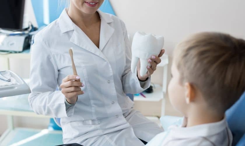 Pediatric dentist showing dental model to young patient in treatment room.