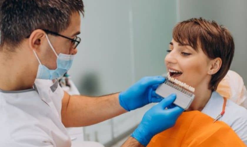 Dentist comparing tooth shade samples with smiling patient during cosmetic dental consultation.