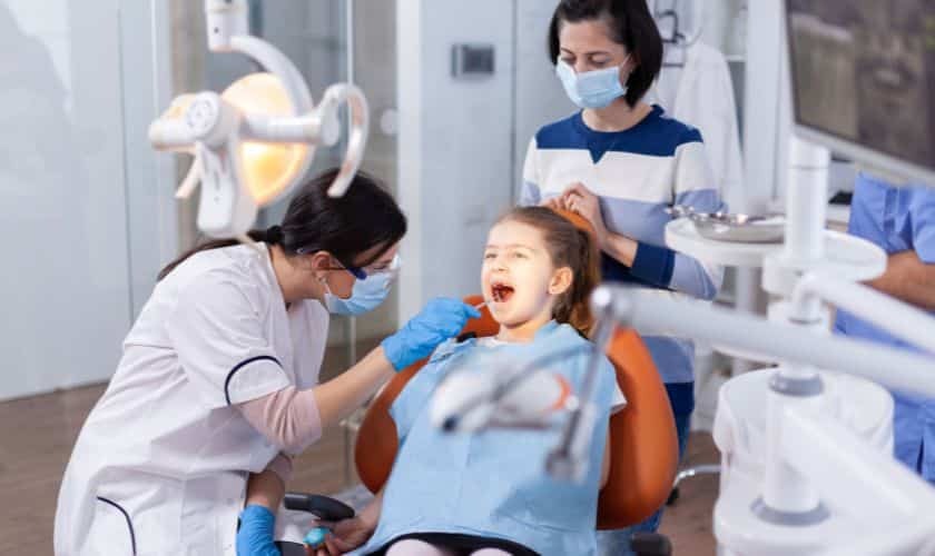 Young girl receiving dental examination from pediatric dentist in treatment room.