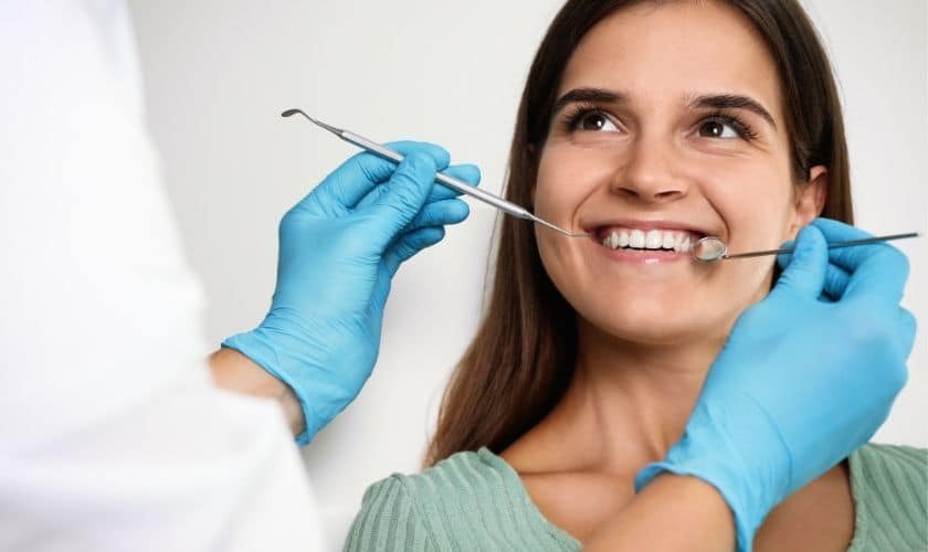 Smiling patient receiving cosmetic dental examination with dental instruments and tools.