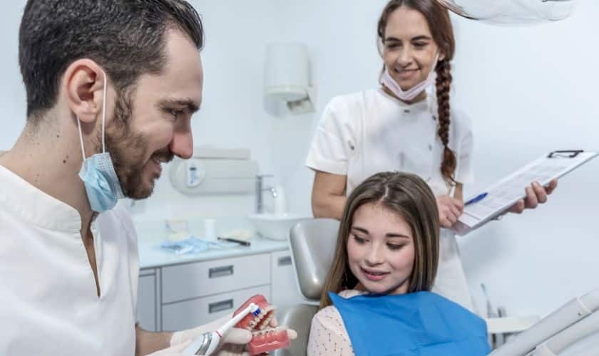 Pediatric dentist showing dental model to young patient in modern treatment room.