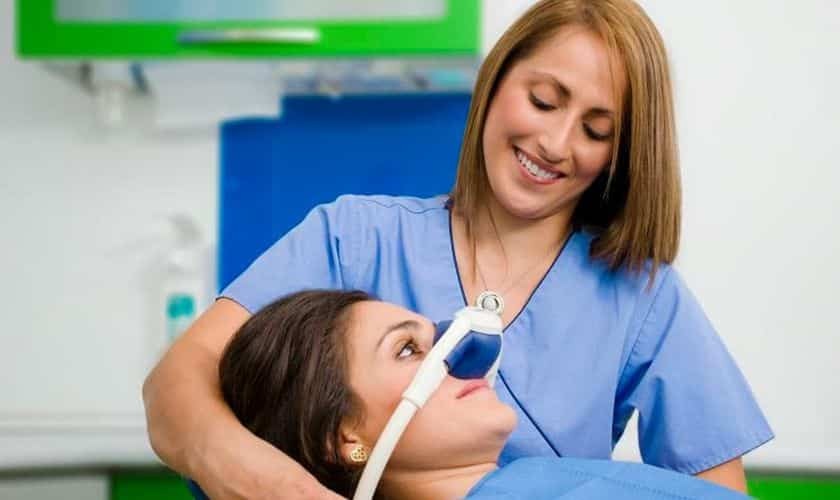 Dentist in blue scrubs comforting anxious patient in dental chair during sedation dentistry treatment.