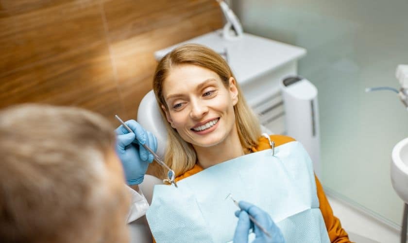 Smiling female dentist holding dental tools while treating patient in dental office.