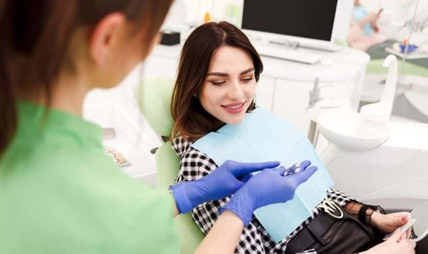 Dentist in blue gloves showing treatment plan to smiling patient in dental office.