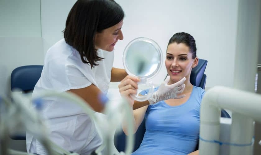 Dentist showing patient mirror reflection during cosmetic dental consultation in treatment room.