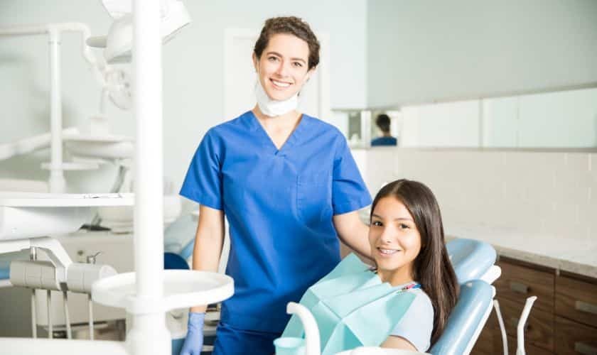 Female pediatric dentist with young patient smiling in modern dental treatment room.
