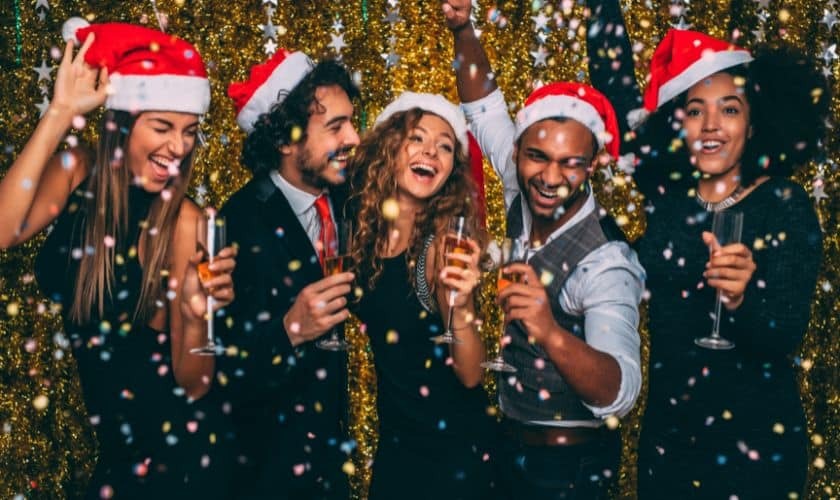 Young adults celebrating Christmas with champagne glasses and Santa hats at a holiday party.
