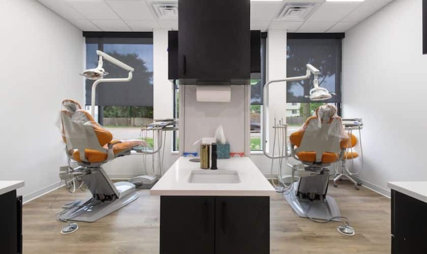 Modern dental treatment room with two orange patient chairs, overhead lighting, and central instrument station at Puyallup p.