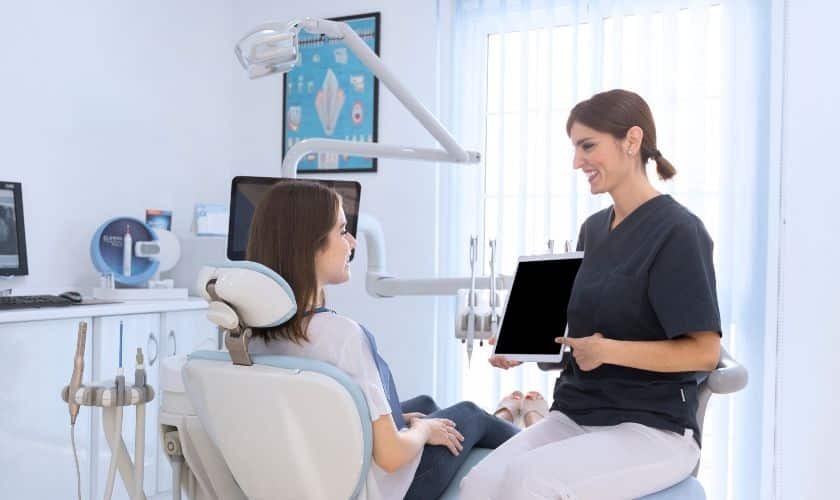 Dentist showing digital tablet to patient in modern dental office treatment room.