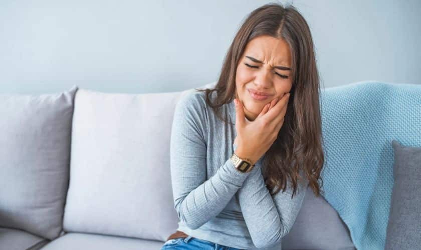 Woman holding her cheek in pain, illustrating dental emergency symptoms and discomfort.