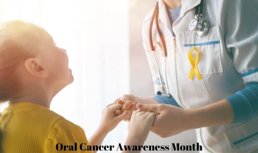 Pediatric patient in yellow shirt holding hands with healthcare provider wearing yellow cancer awareness ribbon during oral.