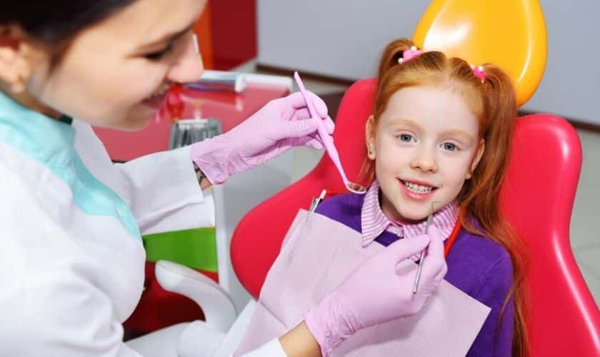 Pediatric dentist examining young girl's teeth in dental chair during routine checkup.