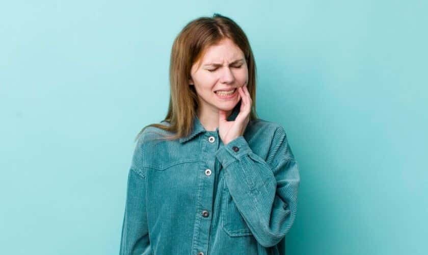 Woman with reddish-brown hair touching her cheek and smiling, wearing a teal button-up shirt against a blue background.