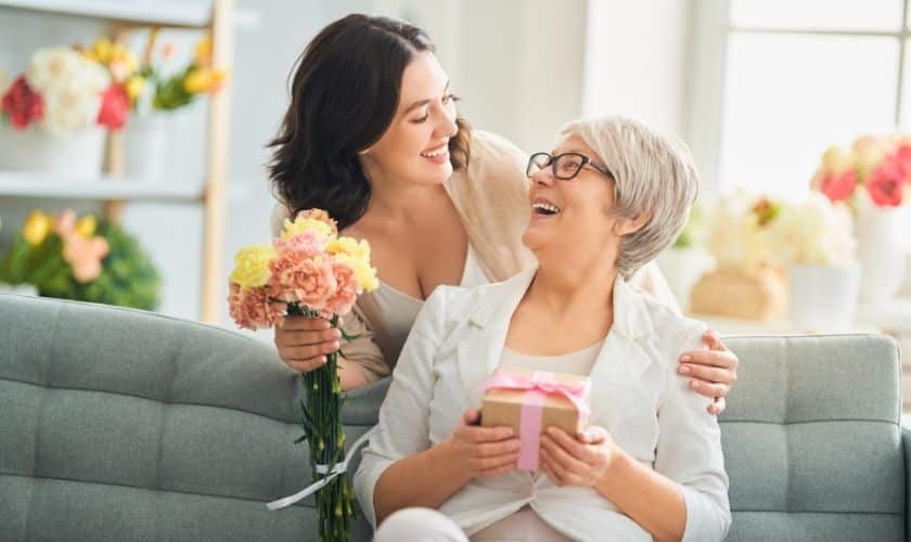 Happy senior mother receiving flowers and gift from adult daughter on Mother's Day.
