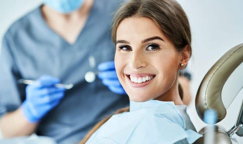 Smiling patient with dentist in background holding dental instruments during cosmetic treatment.