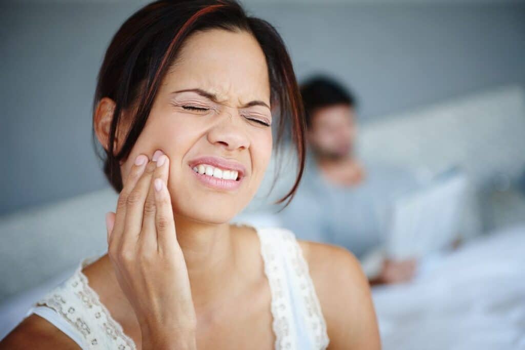 Woman experiencing dental pain, holding her cheek in discomfort.