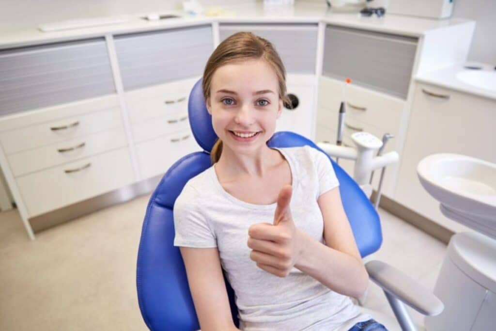 Happy young patient giving thumbs up in modern dental office treatment room.