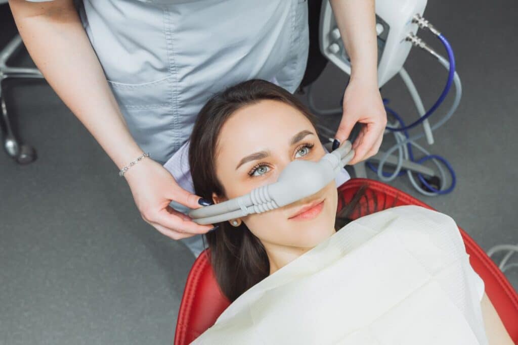 Dentist applying nitrous oxide mask to young patient for sedation dentistry treatment.