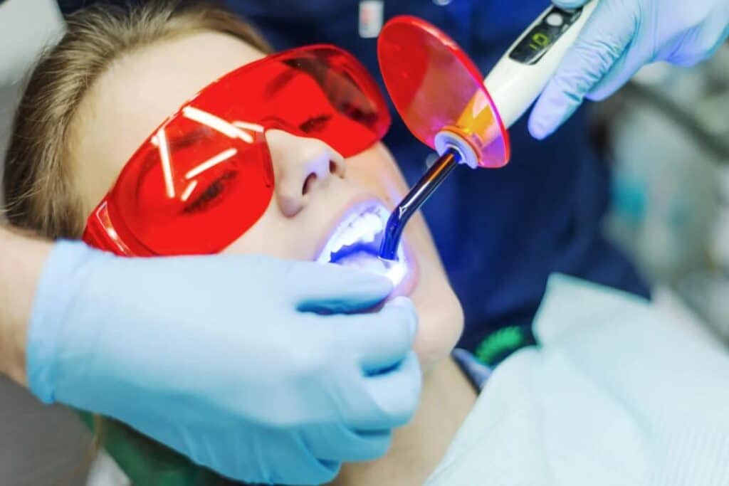 Child wearing red protective eyewear during dental laser treatment with dentist in blue gloves.