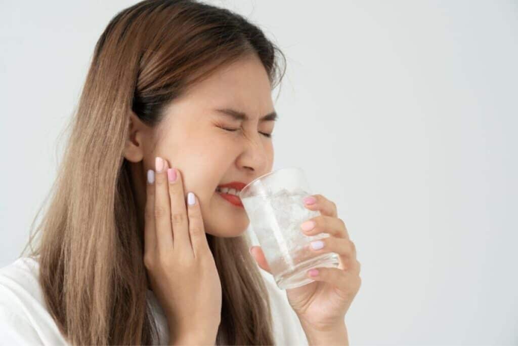 Woman holding glass of water while touching her cheek in pain from a broken tooth.