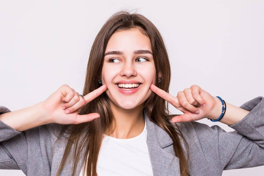 Young woman pointing to her smile after cosmetic dental work in Puyallup.