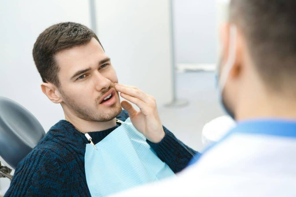 Male patient pointing to his cheek in pain during emergency dental consultation with dentist.