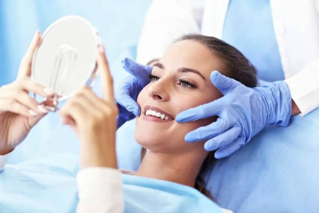 Woman admiring her smile in mirror during cosmetic dental consultation with dentist.