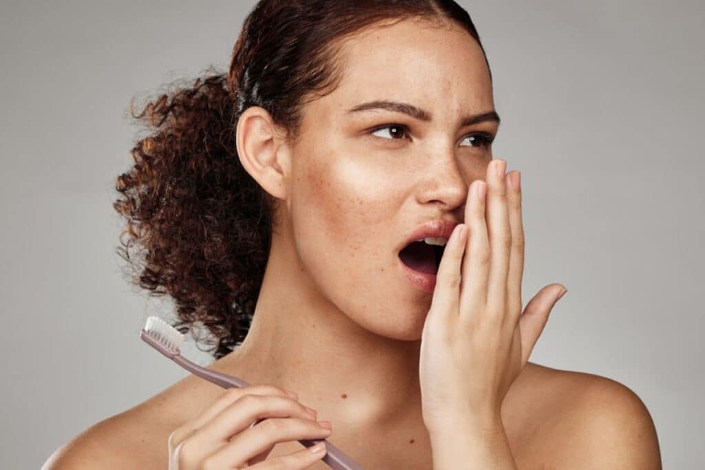 Woman holding toothbrush to cheek, experiencing tooth pain or sensitivity.