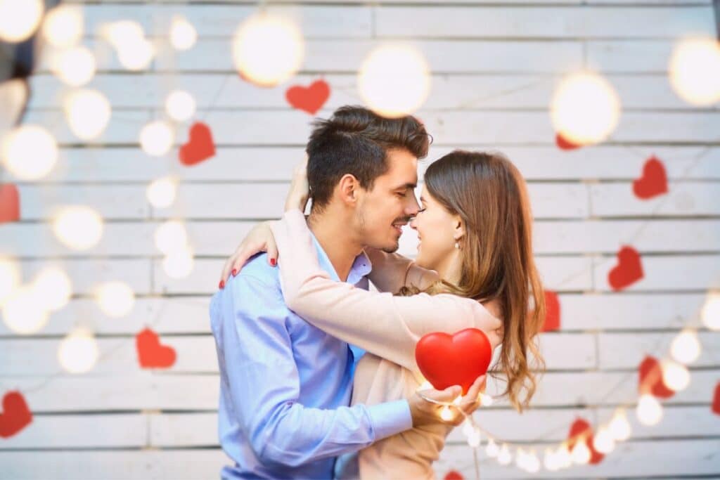 Couple holding red heart with romantic backdrop for Valentine's Day dental health tips.