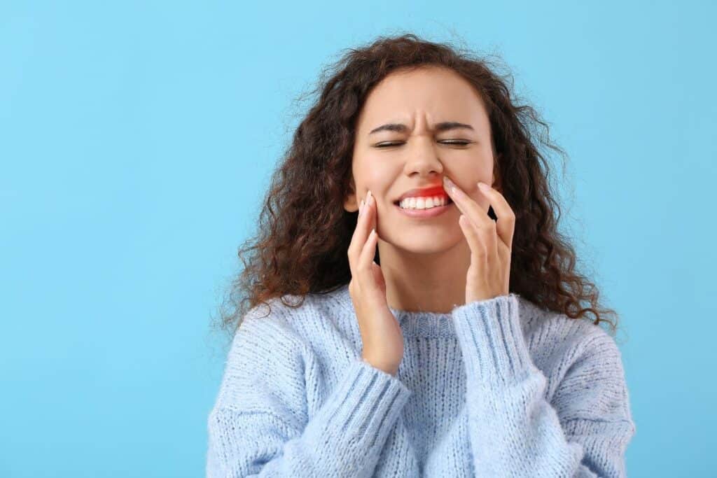 Woman with gum pain touching her cheek, illustrating dental discomfort related to gum disease.