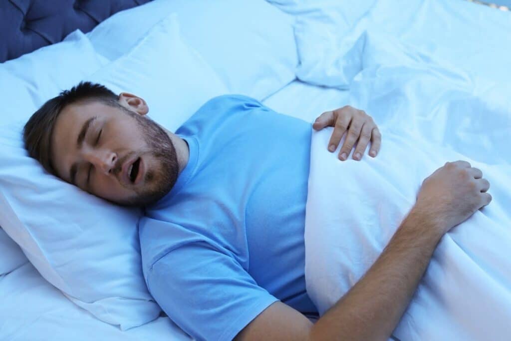 Man sleeping on side with mouth open, illustrating sleep apnea and morning breath concerns.