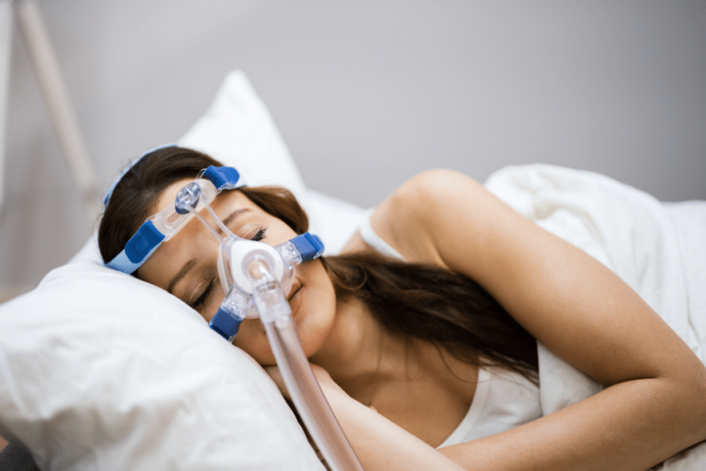 Woman wearing a CPAP mask while sleeping on white pillows for sleep apnea treatment.