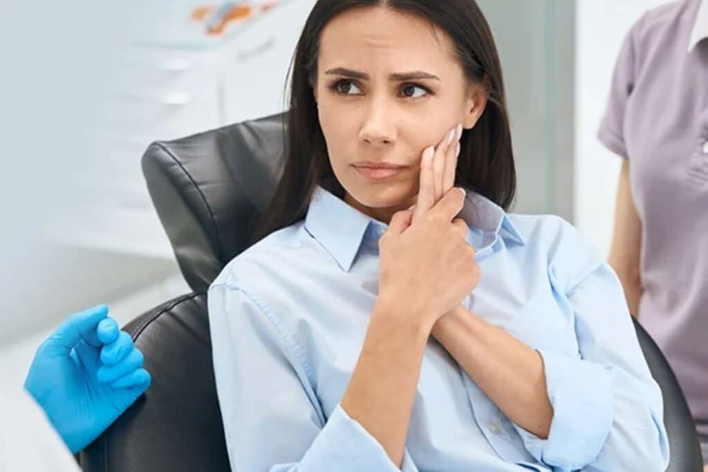 Woman in dental office experiencing tooth pain, holding her cheek during emergency dental consultation.