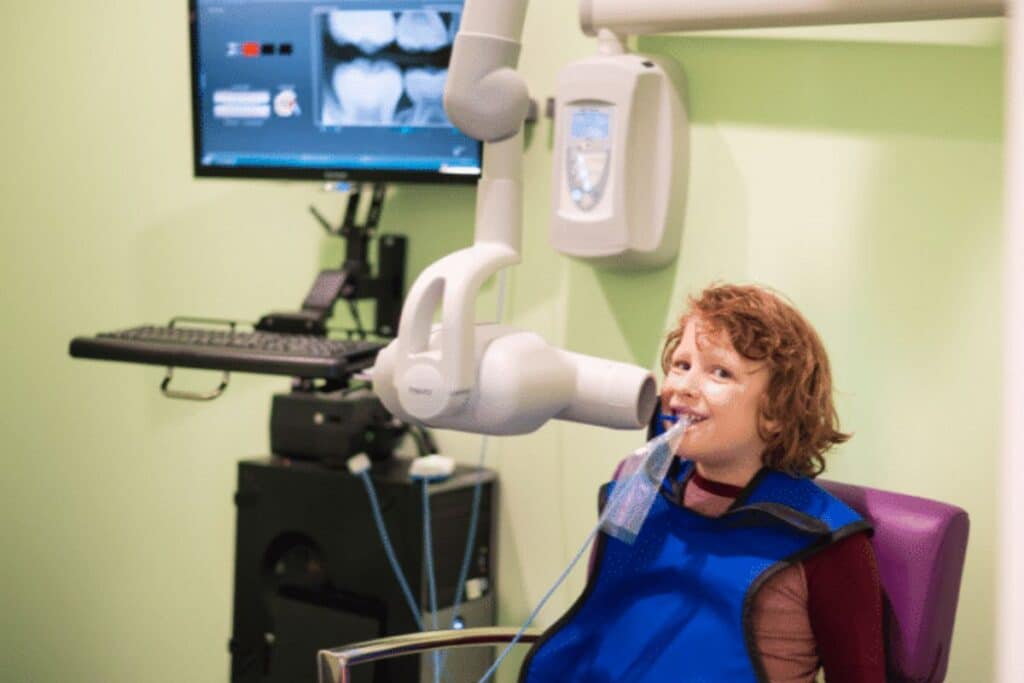 Young patient receiving dental X-ray examination in modern dental operatory with digital imaging equipment.