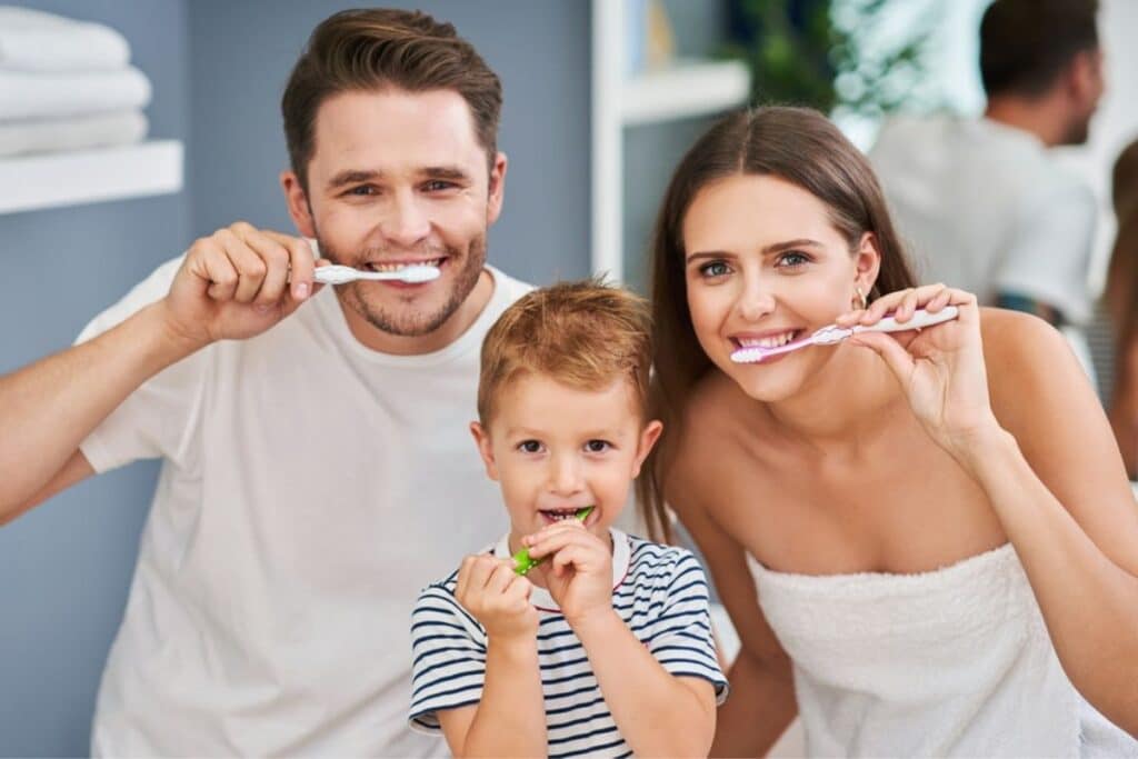 Happy family of three brushing teeth together in bathroom at home.