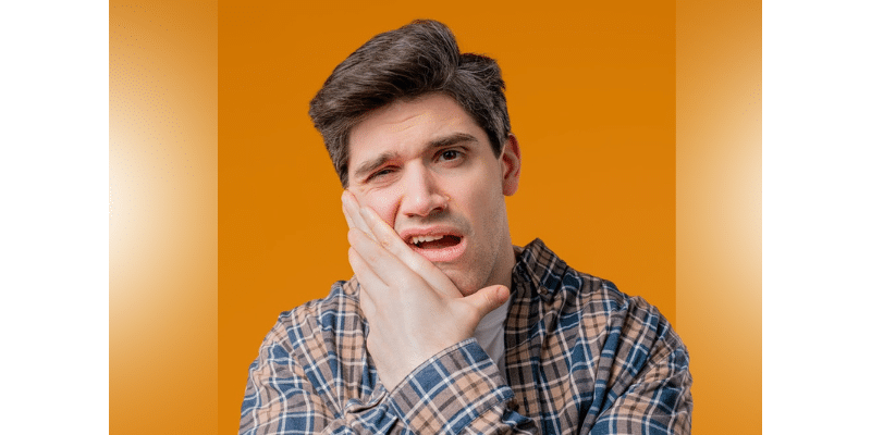 Man holding cheek in pain against orange background, illustrating stress-related dental discomfort.