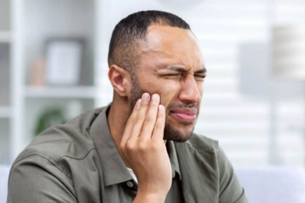 Man holding his cheek in pain, experiencing tooth discomfort that requires dental care.