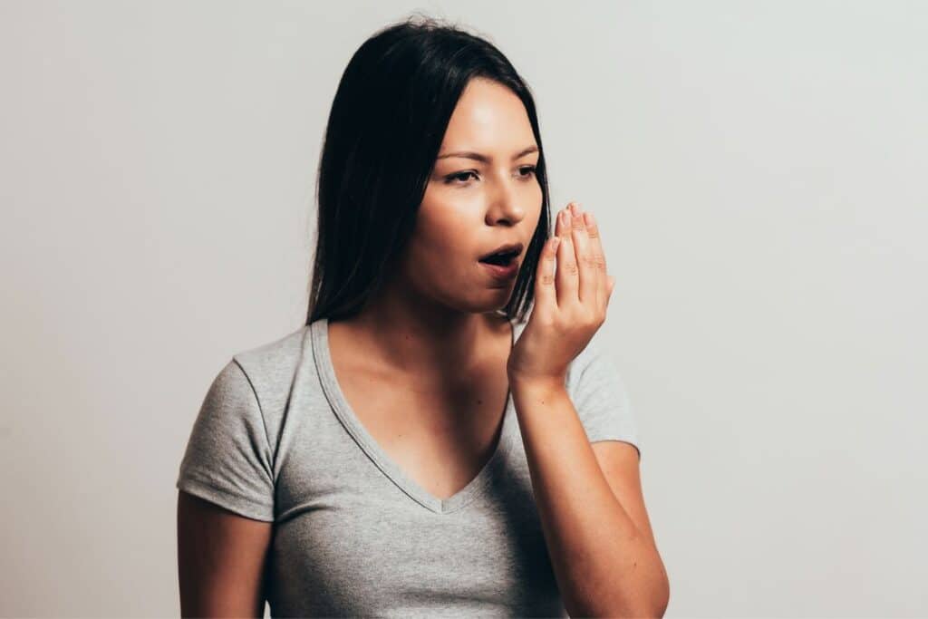 Woman demonstrating bad breath concern by cupping hand near mouth.