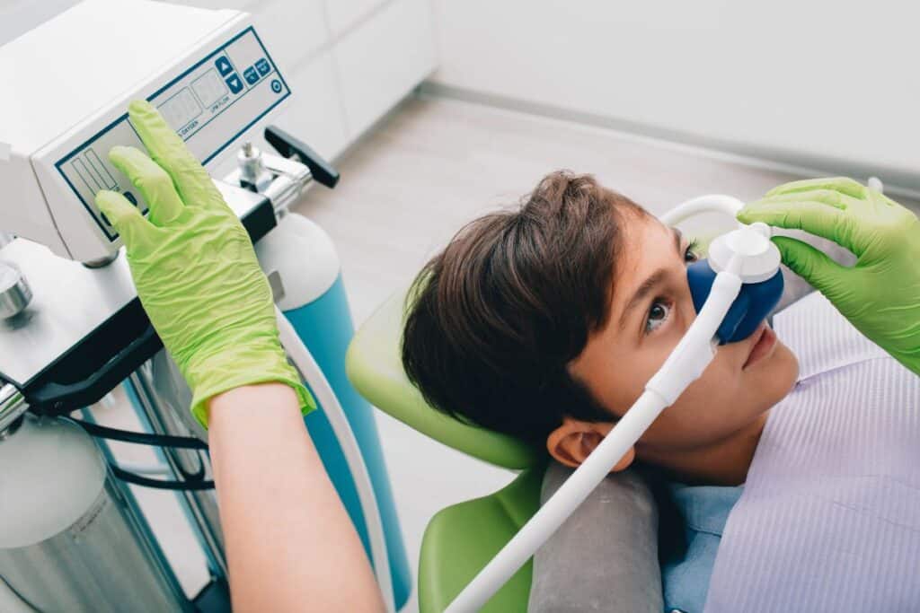 Young patient in dental chair receiving sedation mask during pediatric tooth treatment.