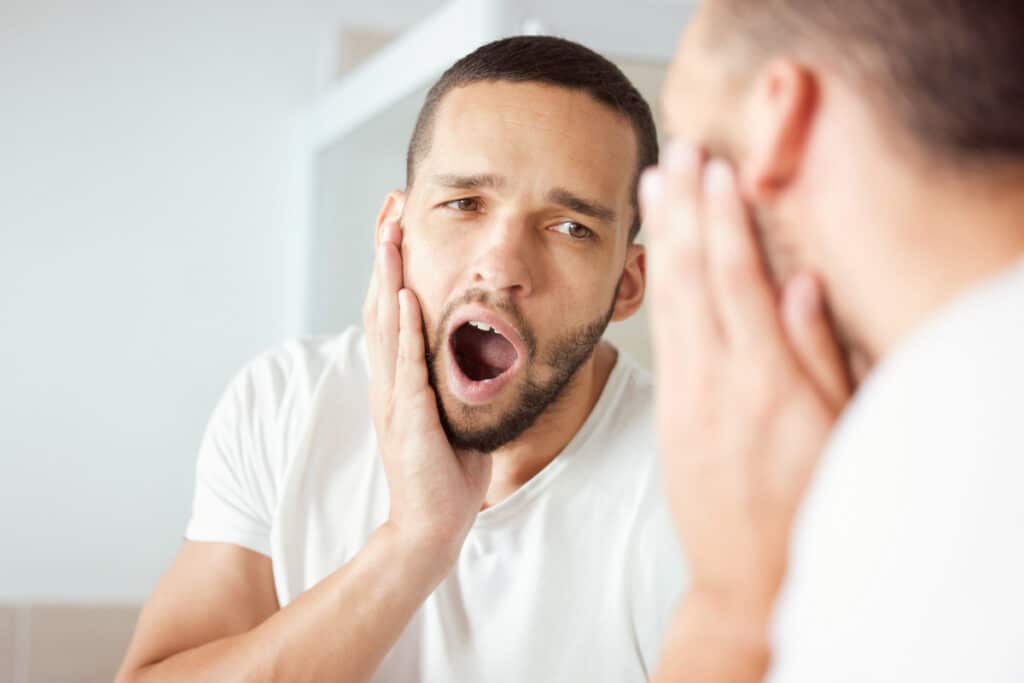 Man examining his open mouth in mirror, checking teeth and gums for dental concerns.