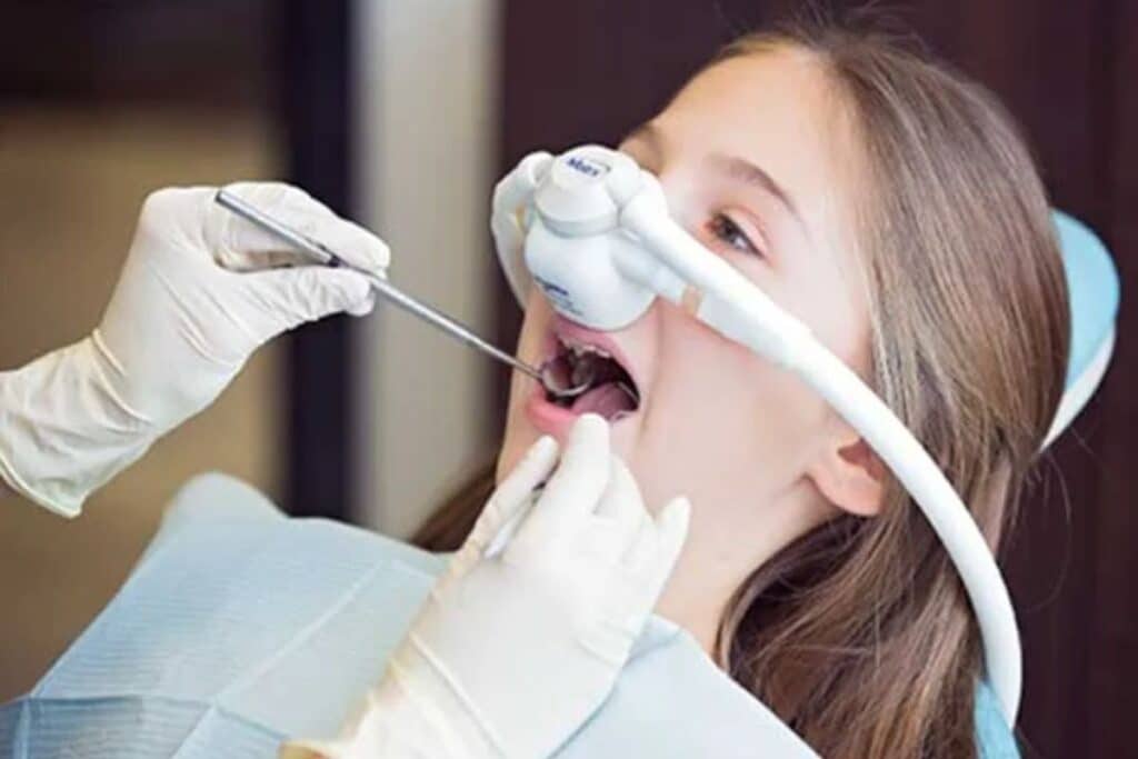 Pediatric dentist examining child's teeth during dental procedure with protective eyewear and instruments.