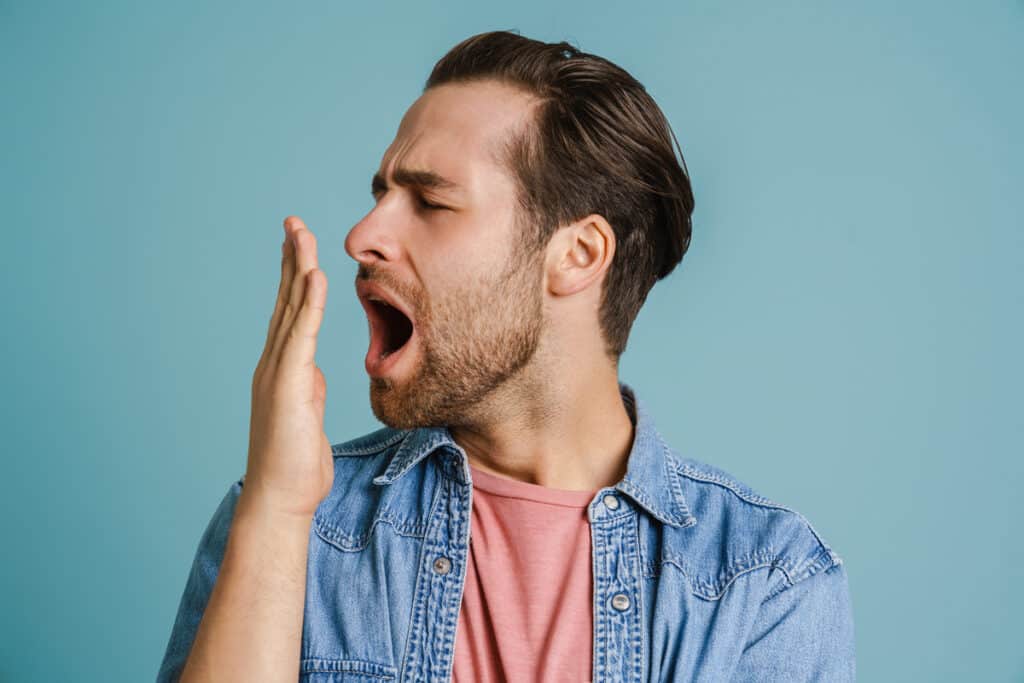 Man checking his breath by holding hand near mouth against blue background.