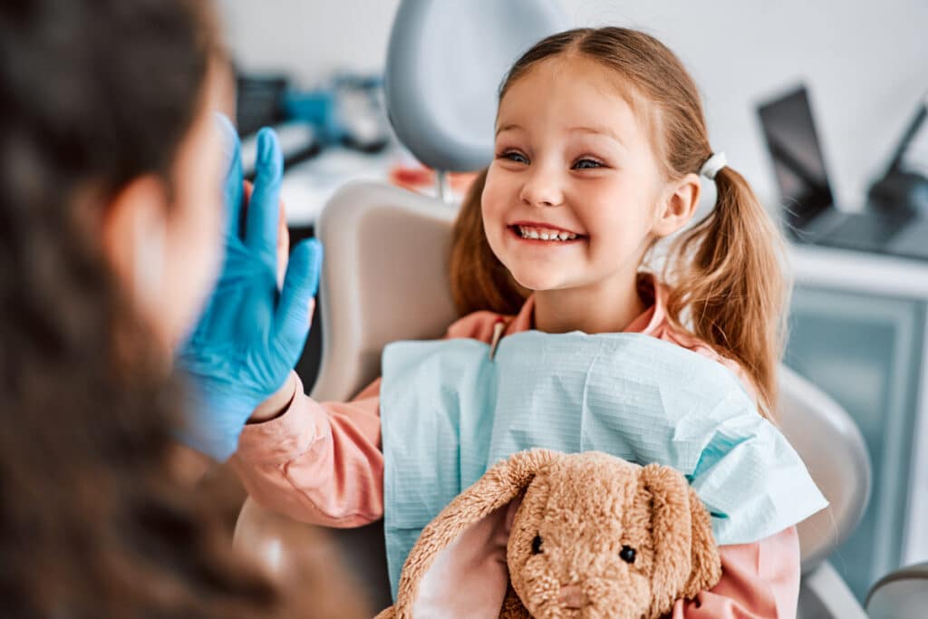 Young girl smiling at pediatric dentist during dental visit while holding stuffed animal.
