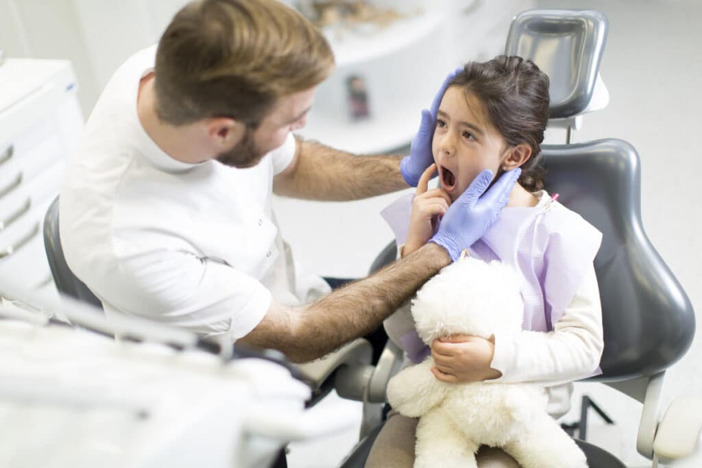 Pediatric dentist examining child's mouth in dental chair during jaw and airway assessment.